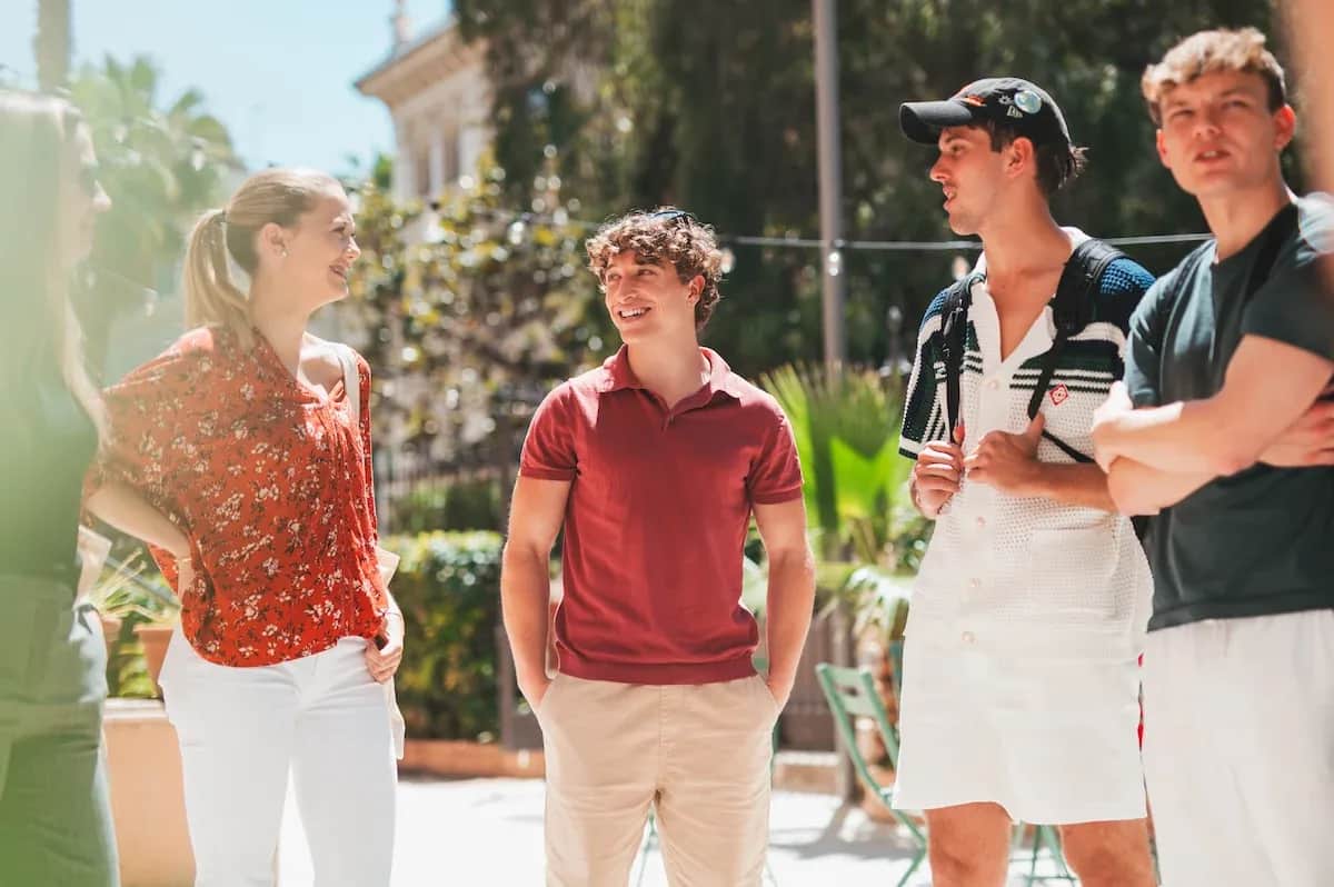 Group of adult students standing outdoors at Expanish, smiling and chatting together under the sun.